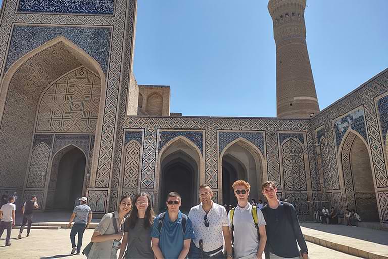 This is a photo of the students taken at the Kalon Mosque in Bukhara, with the Kalon minaret in the background.
